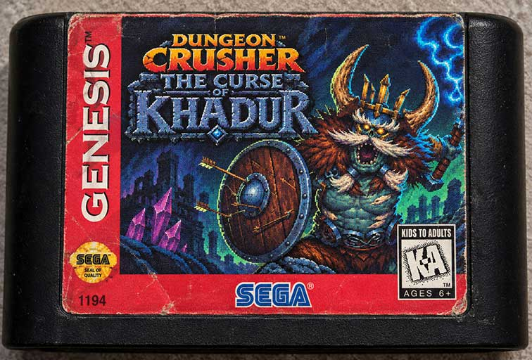 Sega Genesis cartridge of Dungeon Crusher: The Curse of Khadur. The label shows a blue-skinned undead dwarf king with a white moustache, a horned crown and a round shield stuck with arrows, in front of ruined towers and purple crystals under lightning